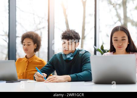 Diverse students focused on their tasks with laptops and notes Stock Photo