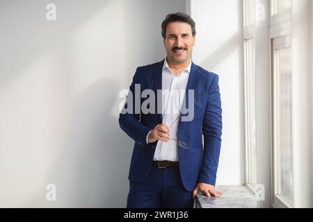 Relaxed and happy middle-aged businessman in a smart blue suit holding eyeglasses Stock Photo
