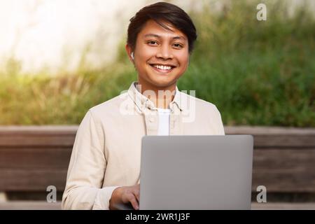 Closeup of cheerful asian guy using computer outdoors Stock Photo