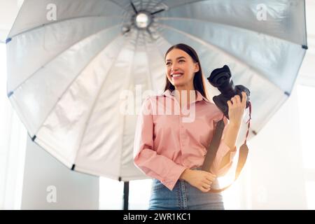 Smiling female photographer with camera in studio Stock Photo