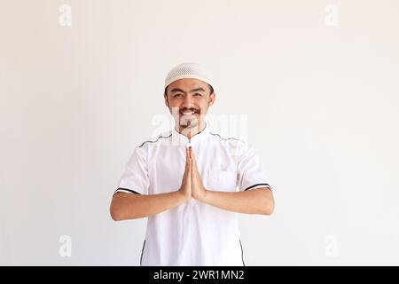 Happy Smiling Young Asian Muslim Man in Baju Koko Standing with Gesturing Eid Mubarak Greeting and Welcoming Ramadan Season. Isolated on White Backgro Stock Photo