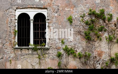 weathered and worn-out window with metal grates on a crumbling brick exterior, framed by rough stone Stock Photo