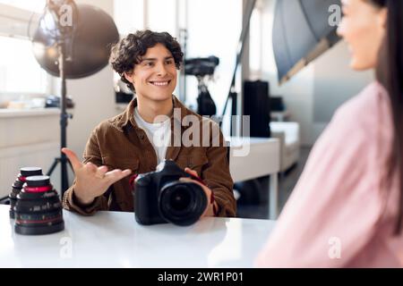 Smiling male photographer holding camera, having conversation with lady model in bright studio Stock Photo