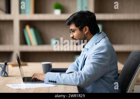 Indian entrepreneur immersed in online tasks typing on laptop indoor Stock Photo