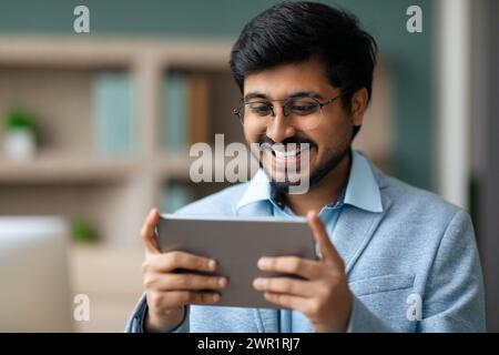 Indian businessman smiles while using application on digital tablet indoor Stock Photo