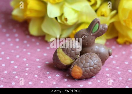 Easter chocolate bunnies and daffodils on pink tablecloth. Bright and colorful Easter card. Stock Photo