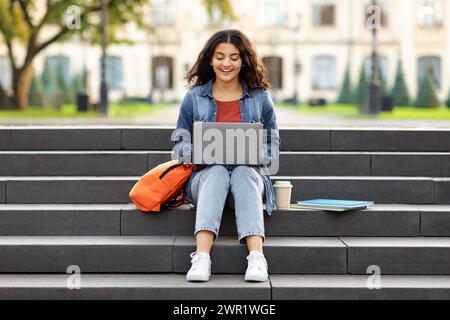 Smiling indian student woman sitting on stairs working on laptop Stock Photo