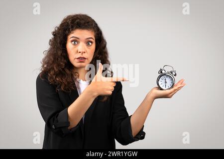 Worried businesswoman pointing at alarm clock Stock Photo