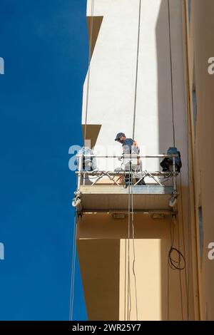 man in a cradle on the side of a building painting. Stock Photo