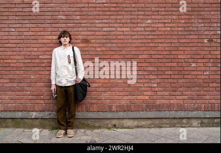 Young man photographer stands with vintage camera against red brick wall, copy space for text. Stock Photo