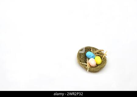 Small model nest with three coloured eggs isolated on a white background. Copy space. Easter theme. Stock Photo