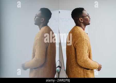 A thoughtful African American man stands in an office, representing concepts like reflection, planning, and strategy in a professional environment. Stock Photo