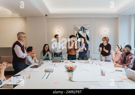 Multi generational, business team celebrating success at modern workplace with applause. Stock Photo