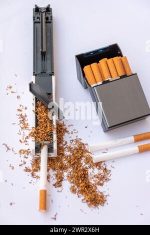 Stuffing machine for cigarette casings filled with tobacco, empty cigarettes on white background, cigarette case with homemade cigarettes. Stock Photo
