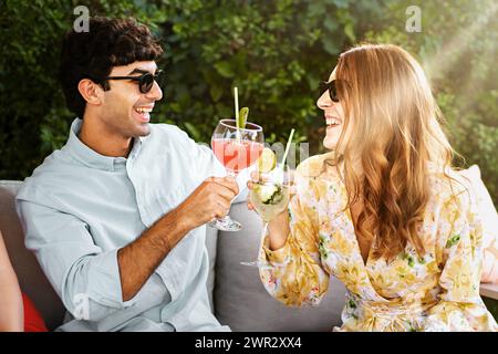 Friends toast with summer cocktails in a garden - Joyful atmosphere as they enjoy refreshing drinks, sharing a sunny moment together. Stock Photo