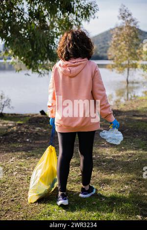 Woman on her back on a sunny day picking up plastic garbage on a volunteering day Stock Photo