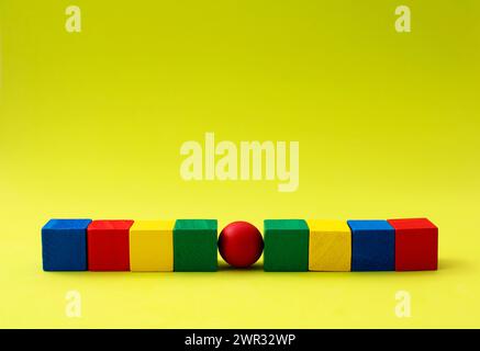Red sphere in the center of row of cubes of different colors Stock Photo