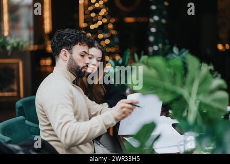 Focused couple reviewing documents together in cozy cafe setting with festive decor. Stock Photo