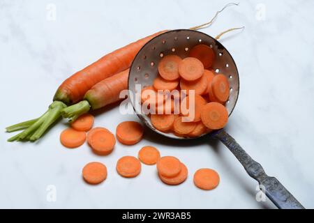 Carrot slices in colander and wooden spoon, Daucus carota Stock Photo
