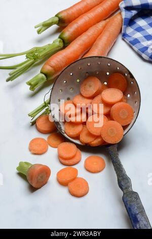 Carrot slices in colander and wooden spoon, Daucus carota Stock Photo