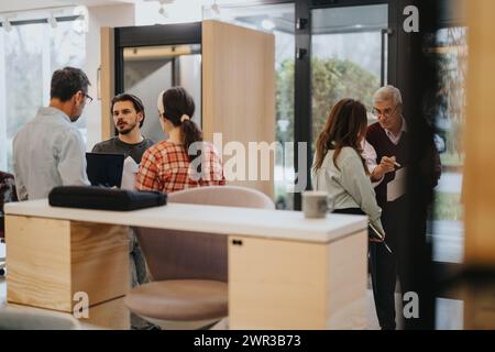 A group of creative business employees discussing over a laptop in a warm, informal cafe setting, with a focus on collaboration. Stock Photo