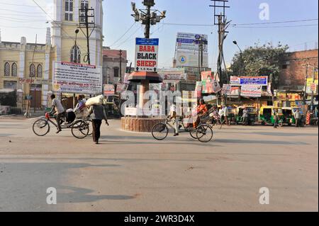 Busy road junction with cyclists and numerous signboards under a clear sky, Varanasi, Uttar Pradesh, India Stock Photo