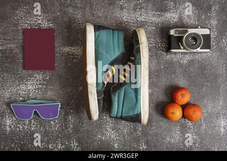 used sports ankle boots with rainbow laces along with vintage photo camera, tangerines, passport and sunglasses Stock Photo