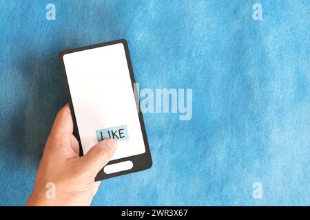 Hand holding a mobile phone paper cutout hitting word like. Social media concept. Stock Photo