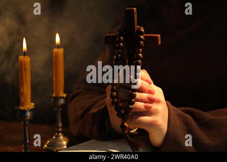 Woman praying at table with burning candles and cross, closeup Stock Photo