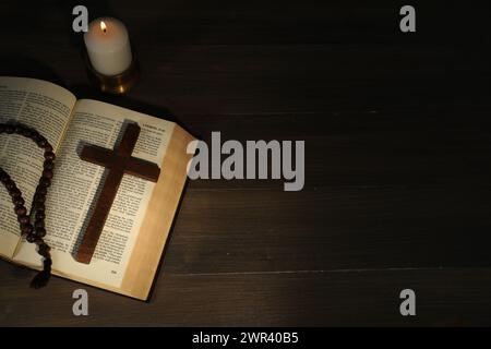 Church candle, Bible, rosary beads and cross on wooden table, top view. Space for text Stock Photo