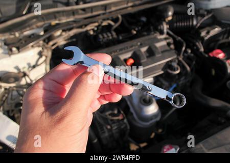 Combination wrench or open end spanner chrome in a car mechanic hand with engine compartment blurred on background, Car repair concept Stock Photo