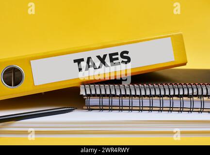 The word taxes written on the label of a yellow binder on the office desk. Stock Photo