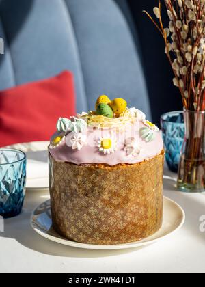 Delicious Easter cake with sugar glaze decorated chocolate eggs and merengue, close up. Festive orthodox easter cake kulich on the table and willow on background Stock Photo