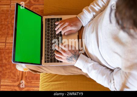 A man on a sofa with a laptop displaying a green screen Stock Photo