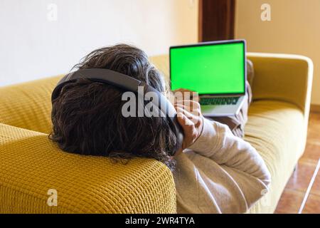 A man on a sofa with a laptop displaying a green screen Stock Photo