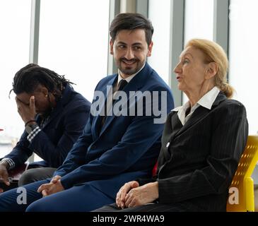 A man in a suit is sitting next to an older woman in a business suit. The man is smiling and the woman is looking at him Stock Photo