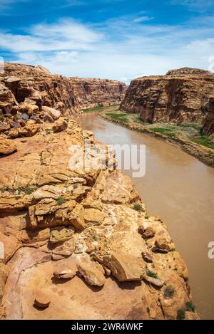 From a rounded sandstone ledge, a muddy brown river flows through a canyon with green banks in Glen Canyon National Recreation Area, Utah. Stock Photo