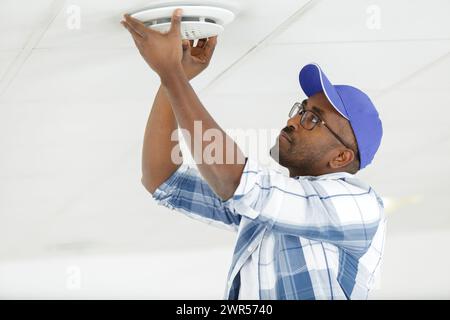 worker installing smoke detector on the ceiling Stock Photo
