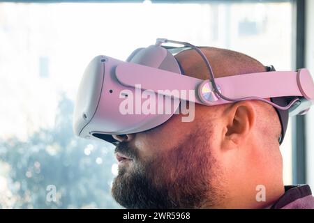 Bearded adult man in virtual reality headset looking up. Overweight male gamer in VR glasses. Modern technology for work, education and entertainment Stock Photo
