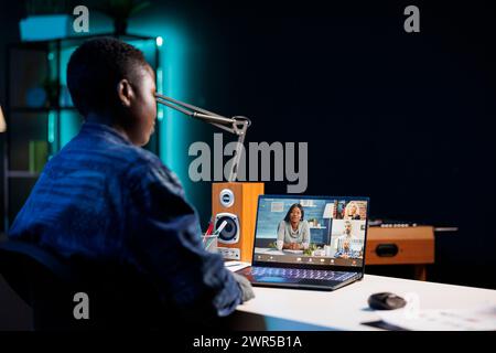Image showing black woman using digital laptop for video call with group of coworkers. African American female blogger attending online webinar, conference meeting on personal computer. Stock Photo