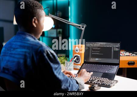 Focused African American woman managing software and programming code on laptop. Skilled female programmer with wireless computer, providing online services and maintaining network security. Stock Photo