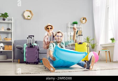 Suitcases packed couple in hats and glasses in living room ready for adventure vacation. Man and woman sits on inflatable mattress suitcases packed Stock Photo
