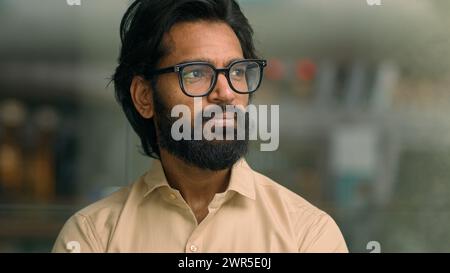 Medium portrait handsome Indian entrepreneur in glasses in creative office look to side thoughtful thinking pondering Arabian man businessman Stock Photo