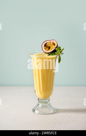 Passion Fruit and mango lassi in traditional tall glass on white and blue background. Healthy beverage made of yogurt, water, fruits and ice. Vertical Stock Photo