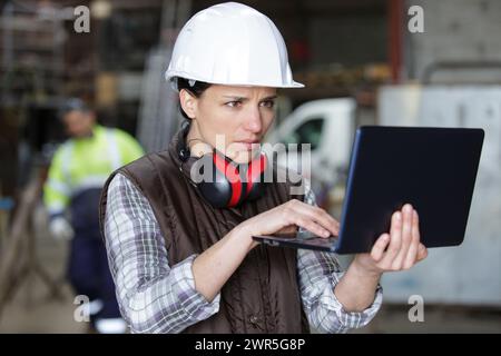 female industrial engineer wearing hard hat uses laptop at factory Stock Photo