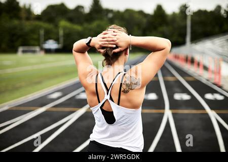 Female runner holding hands behind head on track, Lincoln, Massachusetts, USA Stock Photo