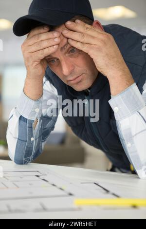 stressed builder worrying over blueprints Stock Photo