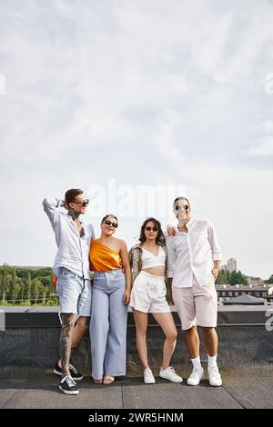 four multiracial cheerful friends with stylish sunglasses posing joyfully on rooftop together Stock Photo