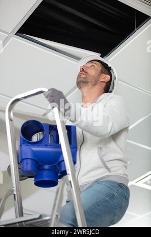 male electrician on stepladder installing ceiling device Stock Photo