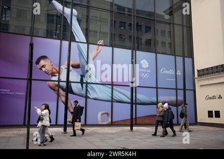 With months before the 2024 Paris Olympics, members of the public pass beneath a huge image of Team GB gymnast and previous Olympic gold medalist, Max Whitlock outside Coutts Bank on the Strand, on 7th March 2024, in London, England. Coutts Bank (and Natwest Bank) are currently Team GB's official corporate partners. Stock Photo